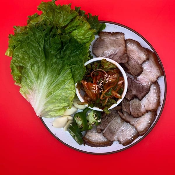 A Korean Bossam platter with sliced pork belly, lettuce, kimchi, garlic, and jalapeños.