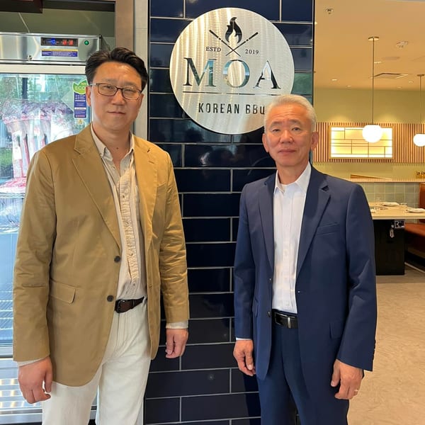 Two men standing in front of the MOA Korean BBQ & Bar logo, with the restaurant interior visible.