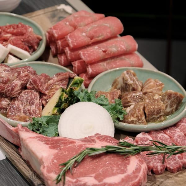 Various cuts of raw Korean BBQ meats, including sliced beef, ribs, and steak, with vegetables.