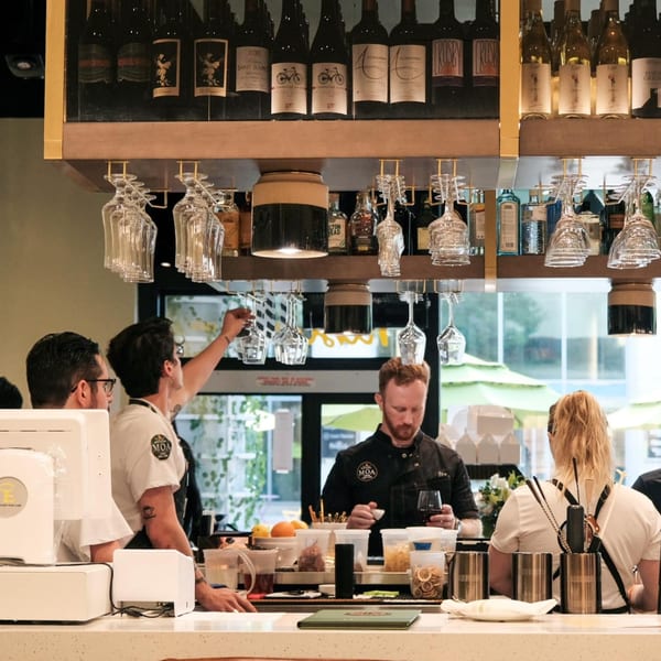 MOA Korean BBQ & Bar bartenders prepare drinks behind a well-stocked bar with wine bottles and glasses.