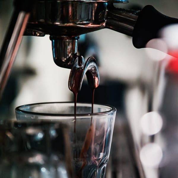 Espresso machine pouring two streams of dark coffee into a clear glass.