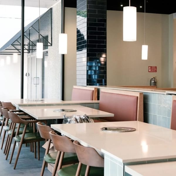 Interior of MOA Korean BBQ & Bar with light tables, pink booths, and modern pendant lights.