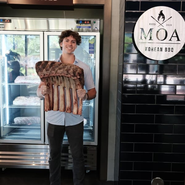 Man holding a large rack of beef ribs in front of a refrigerator at MOA Korean BBQ.