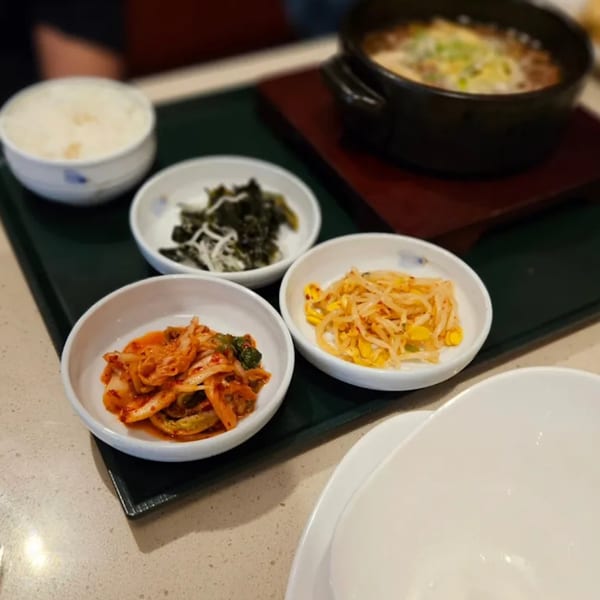 A Korean meal with a bowl of rice, a hot pot, kimchi, and two other side dishes.