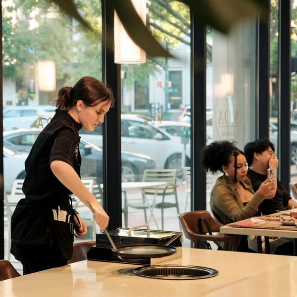 A server at MOA Korean BBQ prepares a grill at a table with customers in the background.