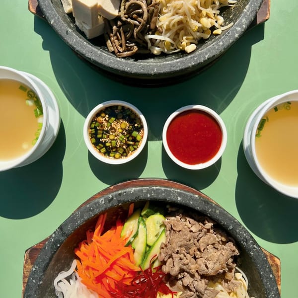 Two Korean bibimbap bowls, one with beef and vegetables, the other with tofu, on a green table.