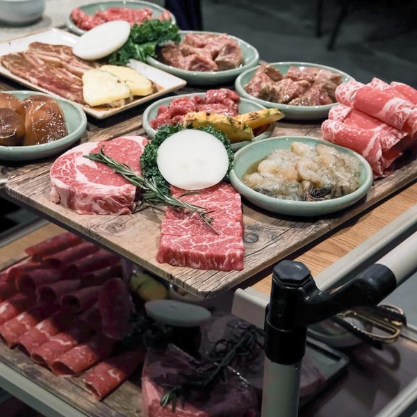 Assortment of raw Korean BBQ meats, including beef, pork belly, and shrimp, on a wooden serving cart.