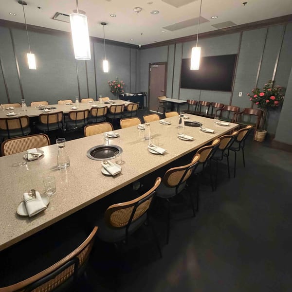 Long dining tables with built-in grills, set with plates and glasses, in a modern private room.