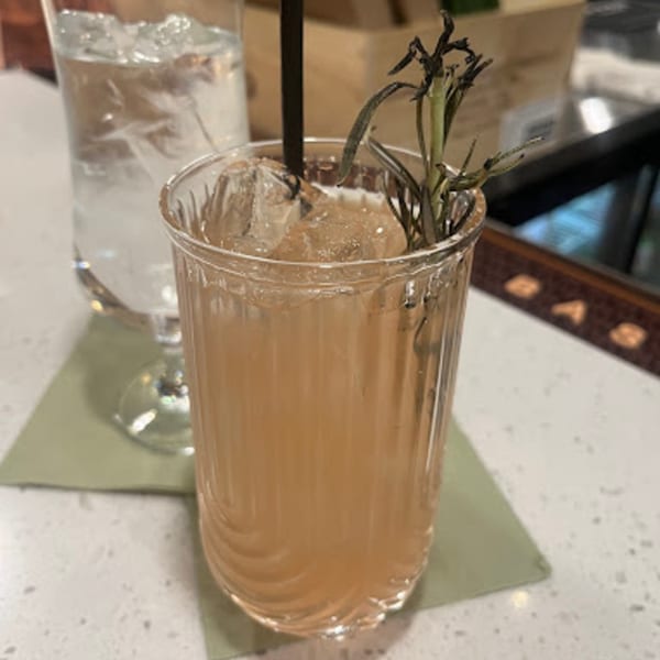 A MOA Korean BBQ & Bar cocktail with ice and rosemary garnish, next to a water glass.